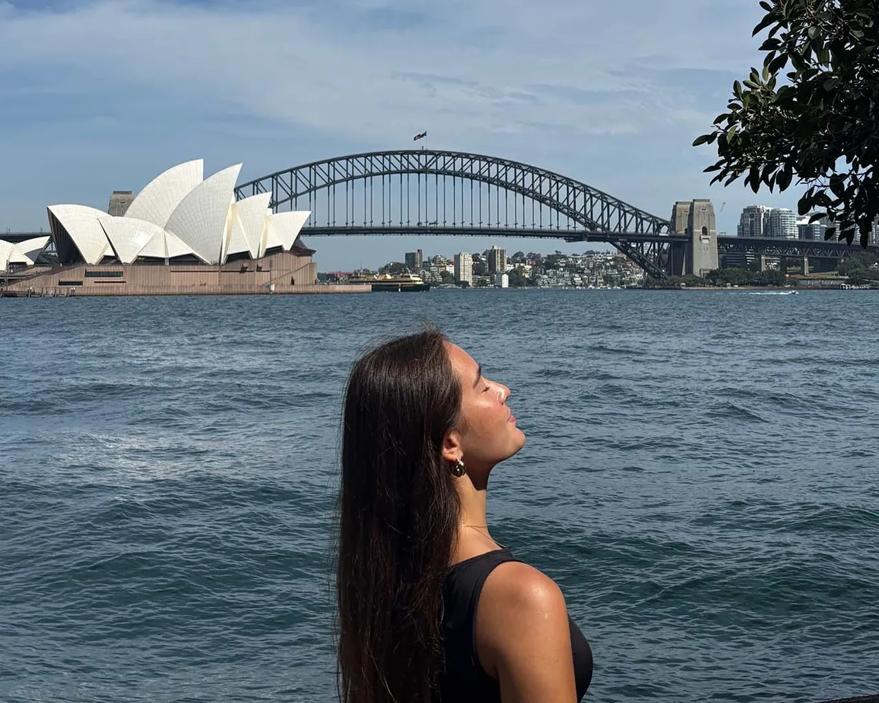 Chica de perfil ante la bahía de Sídney con la Ópera y el Harbour Bridge al fondo