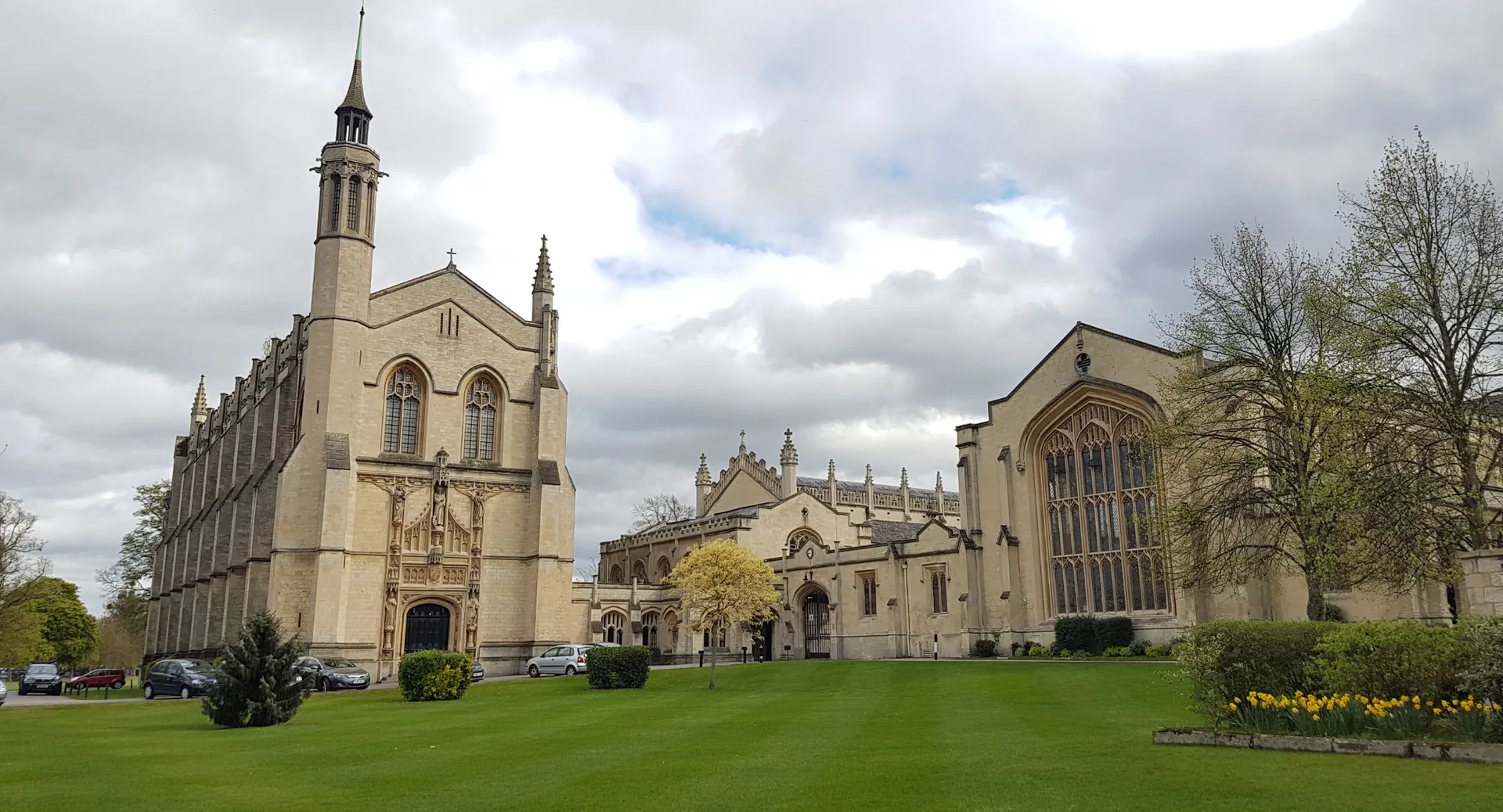 Una maestosa cattedrale gotica con un'alta torre sorge nel cortile verde del Cheltenham College sotto un cielo nuvoloso.