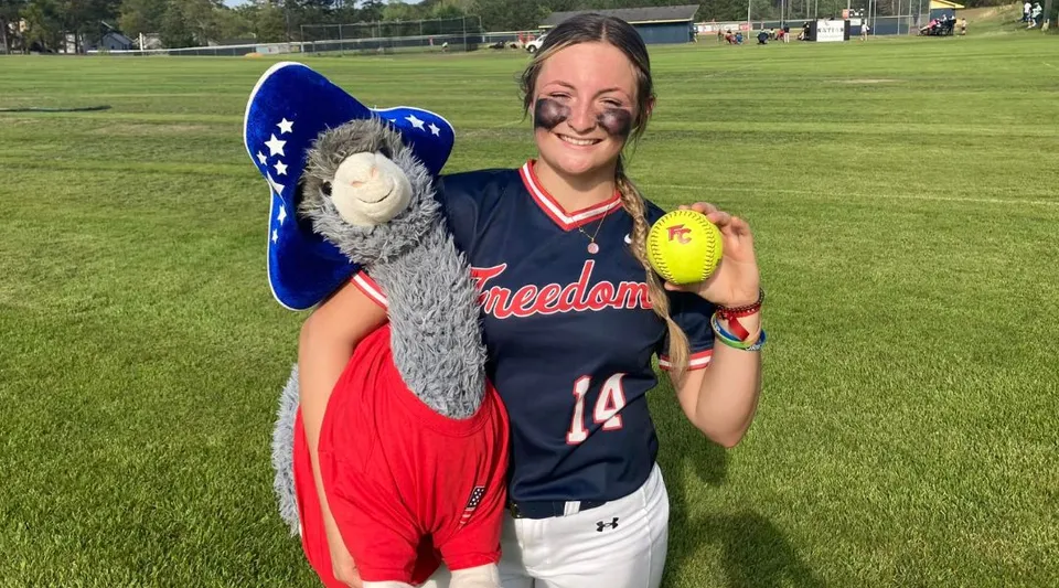 Una studentessa sorridente della Freedom Christian Academy sta sul campo da softball con una palla da softball in mano.