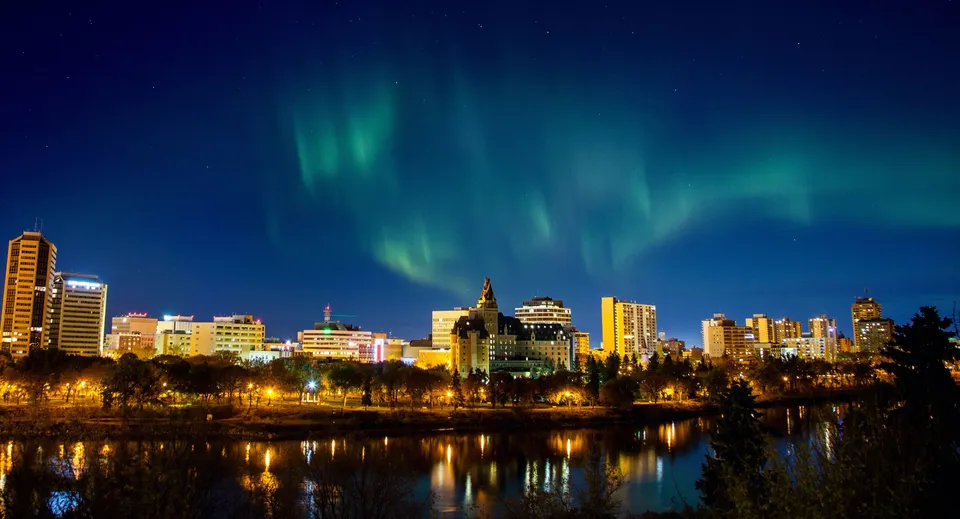 Uno scatto notturno con l'aurora boreale sopra la città che si riflette in uno specchio d'acqua calmo, senza un legame diretto con la Bethlehem High School.