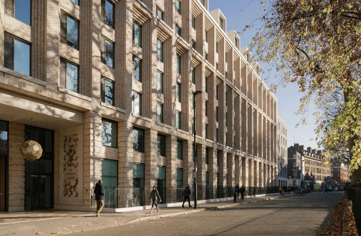 Fachada de piedra clara de un edificio de Londres con peatones en la acera y árboles en otoño