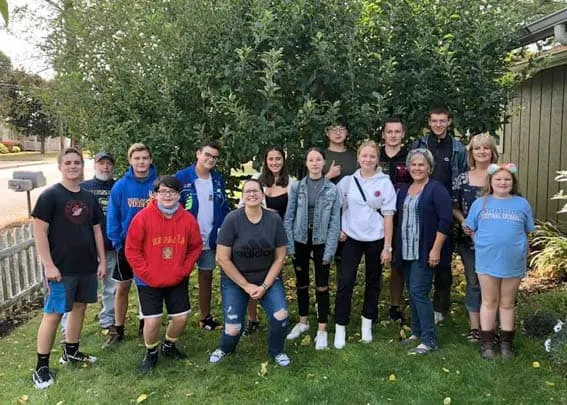 Grupo de jóvenes y adultos posando al aire libre sobre el césped junto a árboles