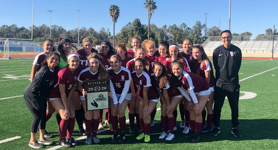 Un gruppo di giovani giocatrici di calcio e il loro allenatore si trovano insieme sul campo da calcio del Torrance Unified School District.