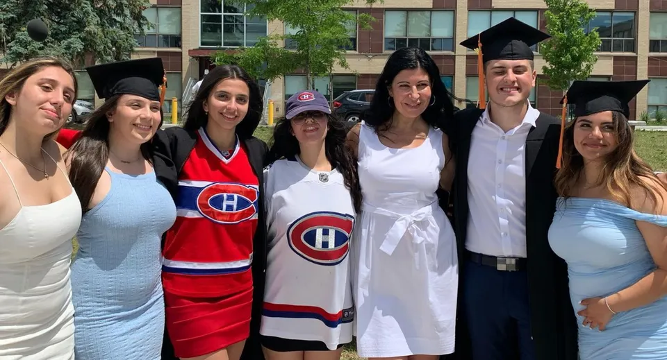 Un gruppo di studenti della LaurenHill Academy con abito da diploma e maglie da hockey sta davanti a un edificio con alberi.