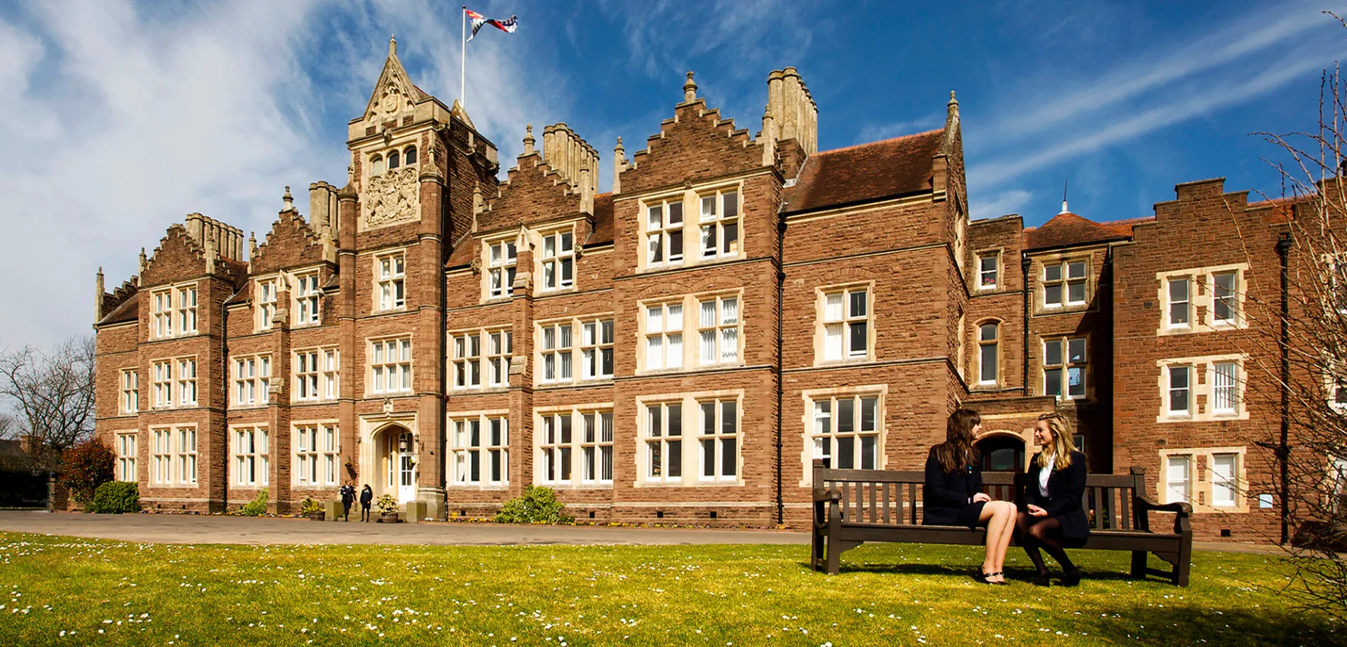 Edificio storico delle Haberdashers' Monmouth Schools su un prato con una persona su una panchina in primo piano.