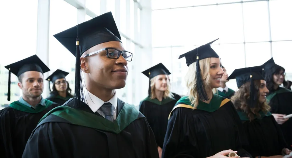 Un gruppo di diplomati e diplomate della Santiam Christian School si trova nella hall davanti a grandi finestre con l'abito accademico.