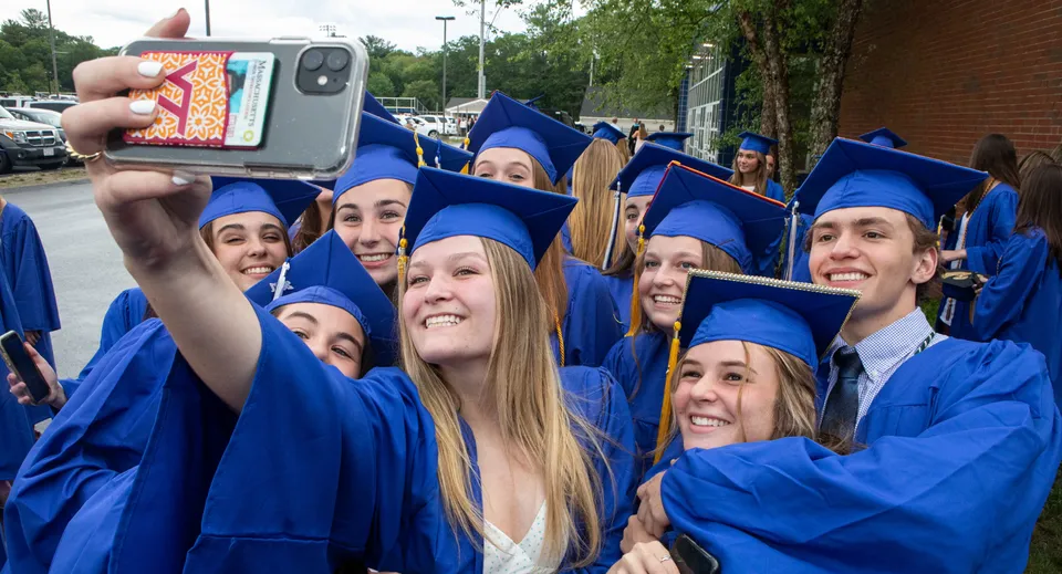 Un gruppo di diplomati della Bedford School in toga blu si mette in posa per un selfie davanti al campus.