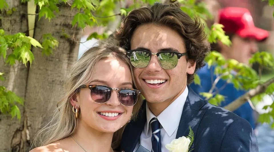 Una coppia sorridente con occhiali da sole si trova davanti a uno sfondo verde di piante nel campus della Northwood School.
