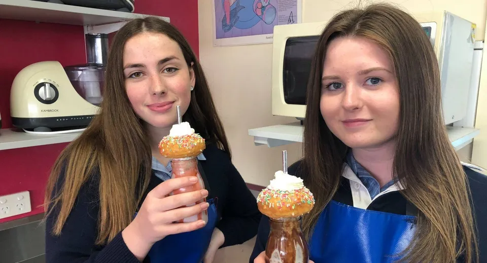 Due studentesse della Queechy High School tengono un gelato in una cucina con decorazioni colorate.