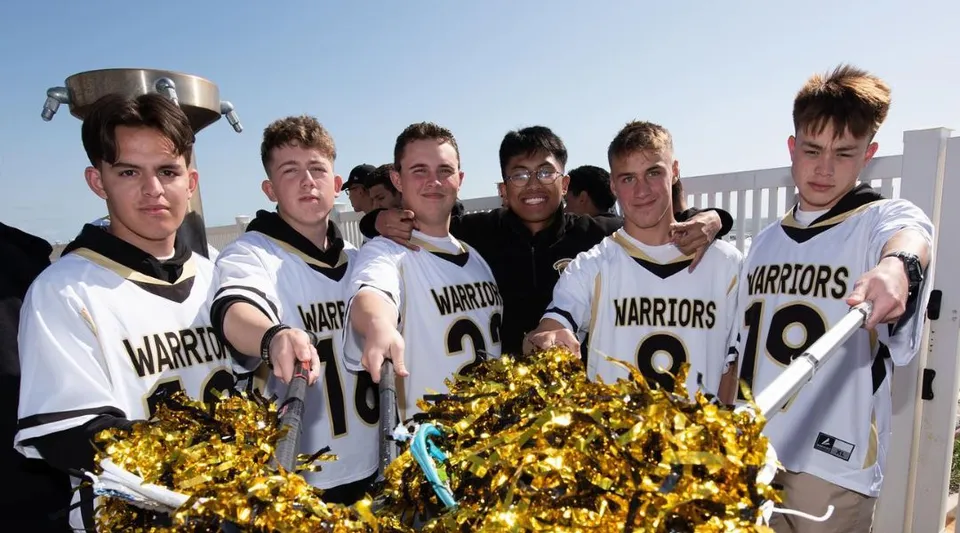 Un gruppo di giovani atleti della Army and Navy Academy si trova all'aperto in divise sportive bianche e nere con la scritta Warriors e tiene in mano pompon dorati.