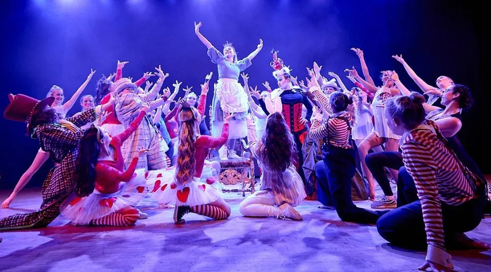 Un gruppo di studenti del Chichester College si esibisce in uno spettacolo teatrale colorato con illuminazione drammatica.