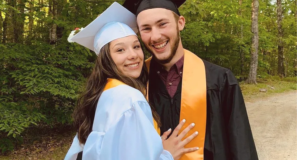 Due diplomate della Lincoln Academy con l'abito da cerimonia si trovano insieme in un'area boschiva con una rigogliosa vegetazione.