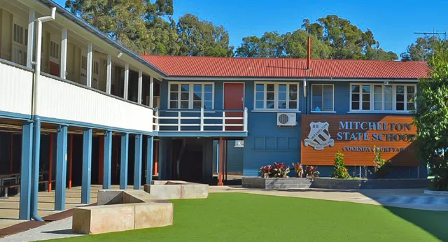 Das Schulgebäude der Mitchelton State High School mit rotem Dach und umgeben von Bäumen und einer Rasenfläche.