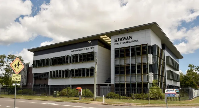 L'edificio a più piani con la scritta Kirwan State High School è circondato da alberi e da una strada.