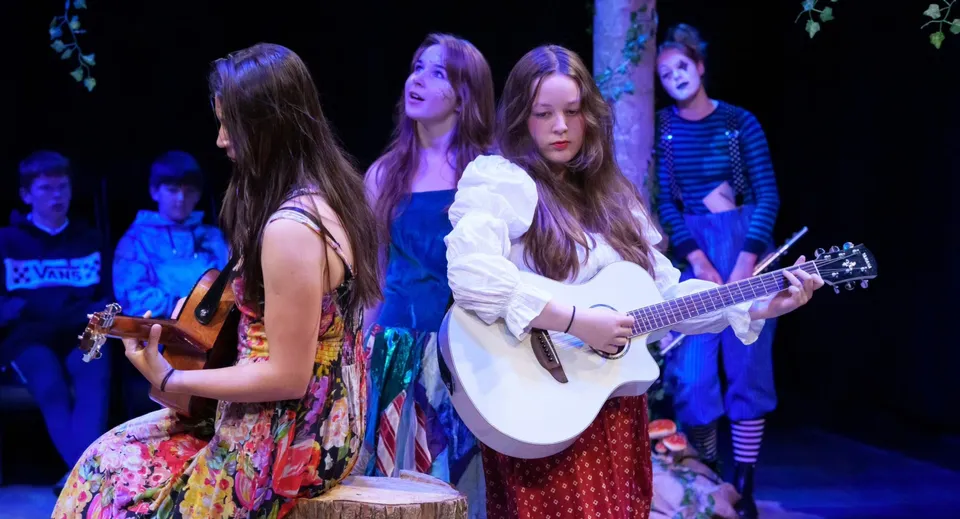 Un gruppo di giovani donne della Bootham School si esibisce con strumenti musicali su un palco con luci colorate.