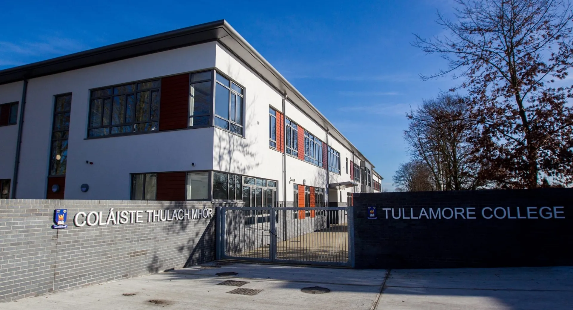 L'edificio moderno a più piani del Tullamore College è circondato da alberi sotto un cielo azzurro e limpido.