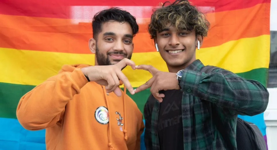 Due studenti dell'Aorere College posano davanti a uno sfondo color arcobaleno e sorridono.