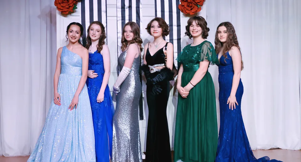 Un gruppo di sei studentesse in abito da sera formale sta davanti a una decorazione floreale rossa sul campus della Webb School.