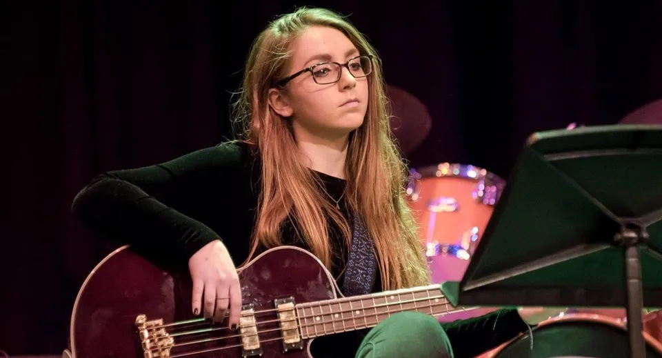 Una studentessa della Leighton Park School suona una chitarra elettrica su un palco davanti ad attrezzature musicali.