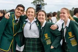 Cuatro estudiantes de la Macarthur Anglican School sonríen juntos al aire libre vistiendo el uniforme escolar verde.