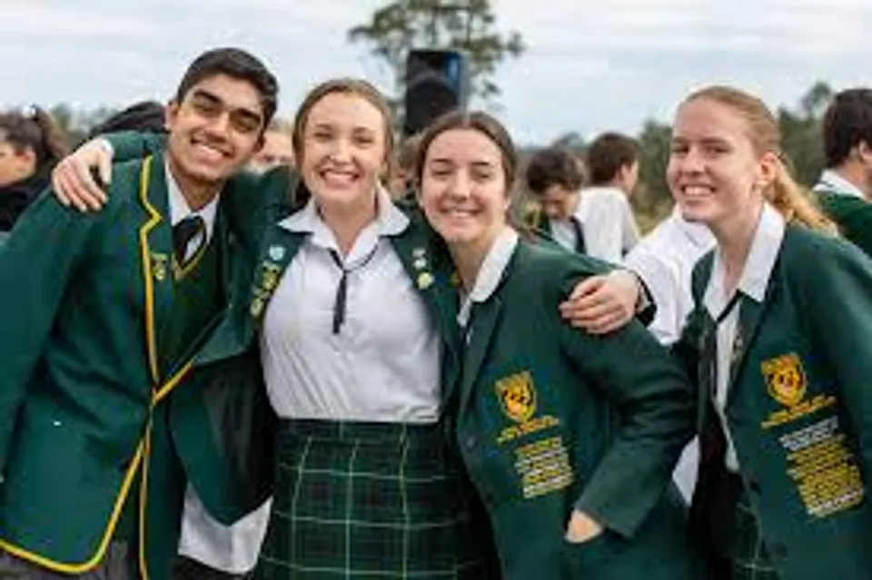 Quattro studenti della Macarthur Anglican School sorridono insieme all'aperto indossando la divisa scolastica verde.