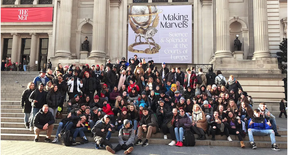 Un grande gruppo di studenti e studentesse si riunisce davanti all'edificio della Centennial Regional High School con lo striscione 'Making Miracles'.
