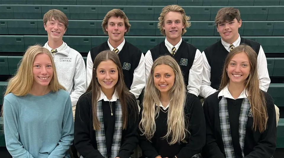 Un gruppo di studenti della Muskegon Catholic Central High School posa insieme davanti a una parete verde all'interno dell'edificio scolastico.
