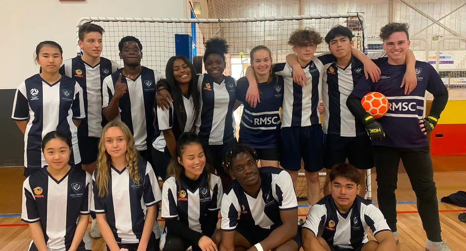 Un gruppo di studenti del Roma Mitchell Secondary College posa insieme in una palestra con una rete da pallavolo sullo sfondo.