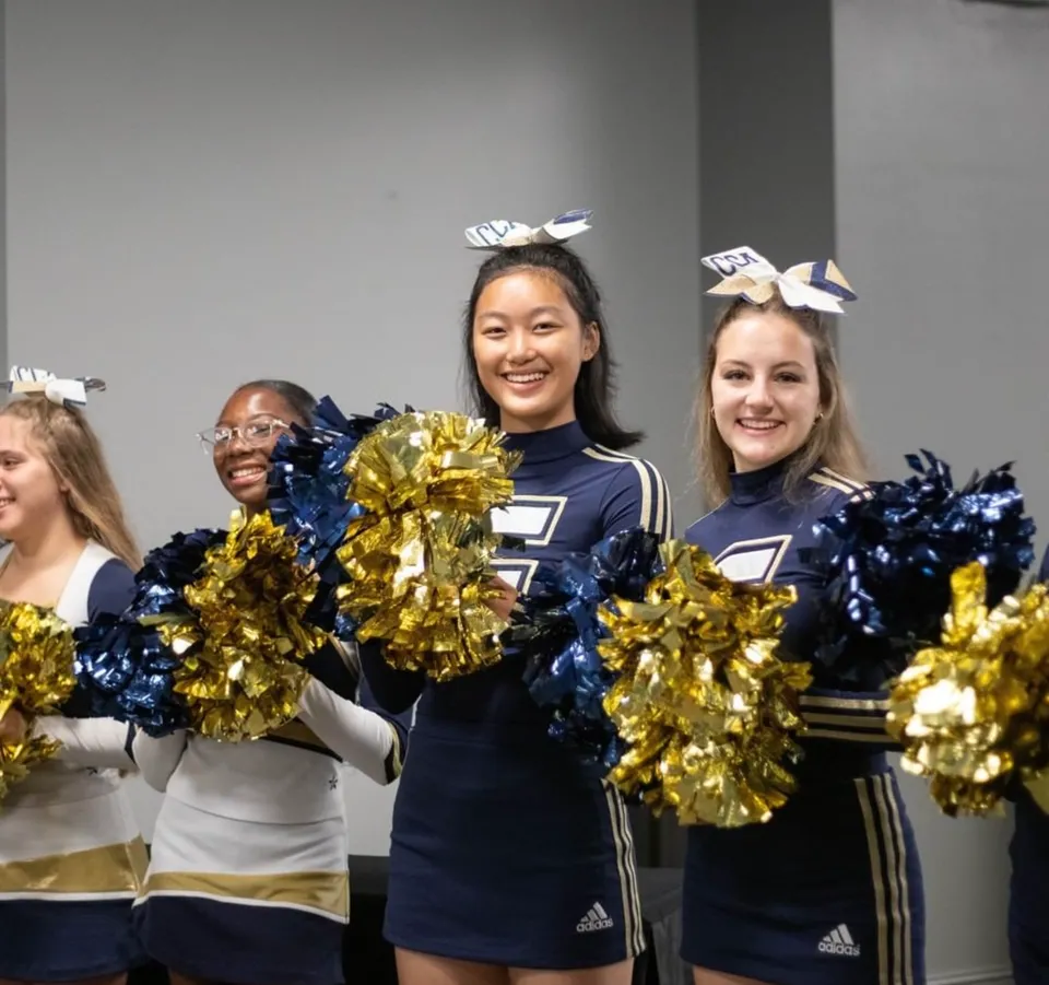 Un gruppo di cheerleader in uniforme blu marina e oro con pompon posa insieme sul campus della Calvary Christian Academy.