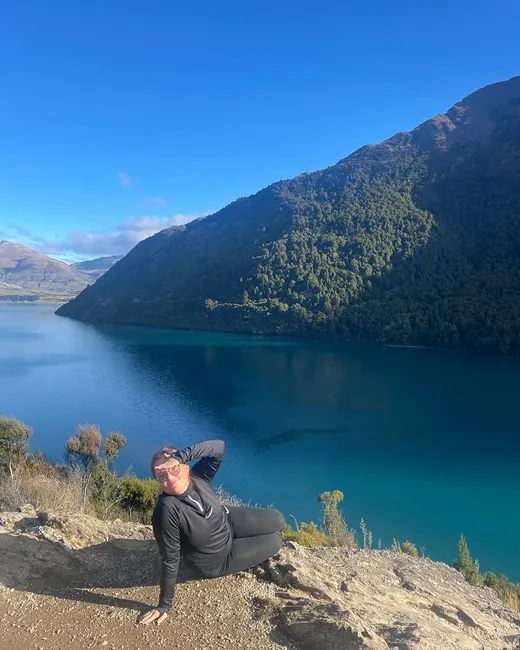 Chica sentada en una roca sobre un lago de aguas turquesas rodeado de montañas boscosas
