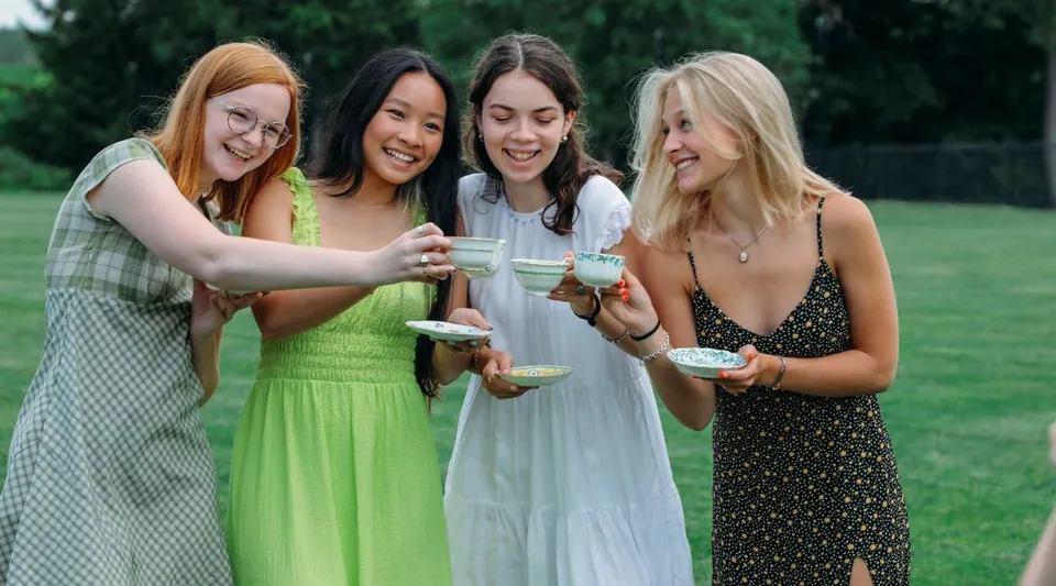 Quattro studentesse della Emma Willard School si trovano insieme all'aperto su un prato con alberi sullo sfondo e tengono in mano delle bevande.