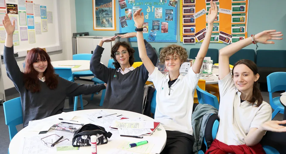 Studenti della The Wren School alzano le mani in classe durante un'attività di lezione.