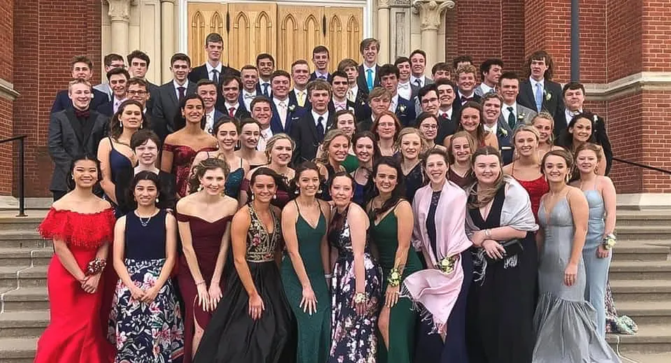 Un grande gruppo di studenti della Beckman Catholic School si raccoglie in abbigliamento formale sulle scale di un edificio storico.
