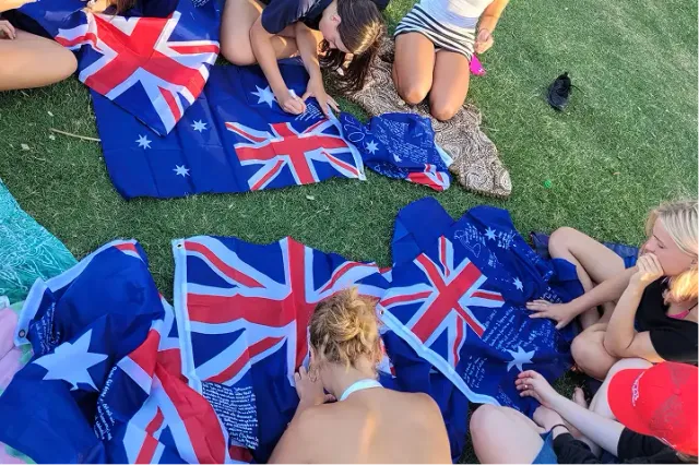 Studenti firmano bandiere australiane seduti sull'erba