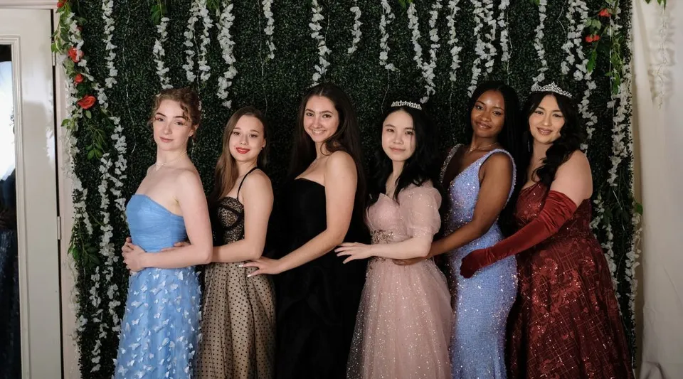 Cinque giovani donne della Maharishi School posano insieme davanti a uno sfondo floreale indossando diversi abiti eleganti.