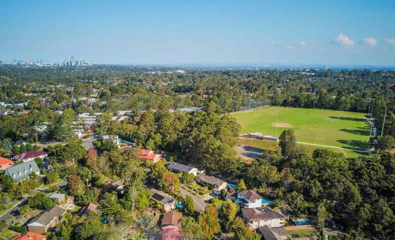 Vista de una superficie verde abierta con bosque y viviendas al fondo de la Ravenswood School for Girls.
