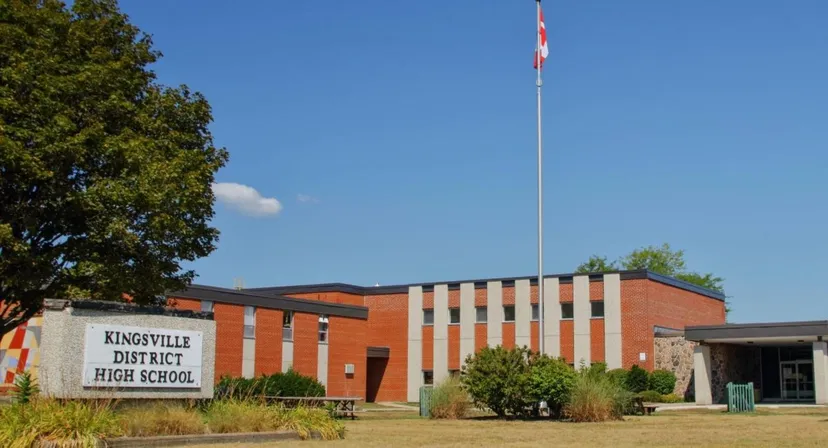 L'edificio in mattoni della Kingsville District High School si trova circondato da alberi e aree verdi con un alto pennone per la bandiera.