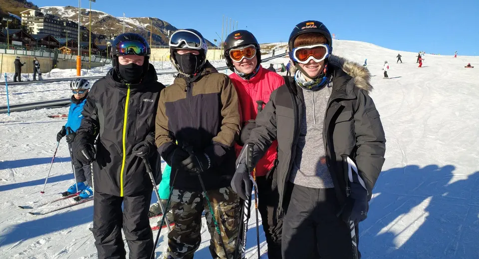 Un gruppo di quattro studenti della Portmarnock Community School sta in piedi in abiti invernali su un pendio innevato davanti alle montagne.