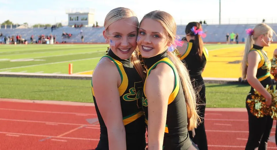Due cheerleader della Bishop Carroll High School posano insieme sul campo sportivo davanti a uno stadio.