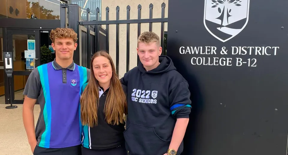 Tre studenti sono in piedi davanti all'insegna del Gawler and District College.