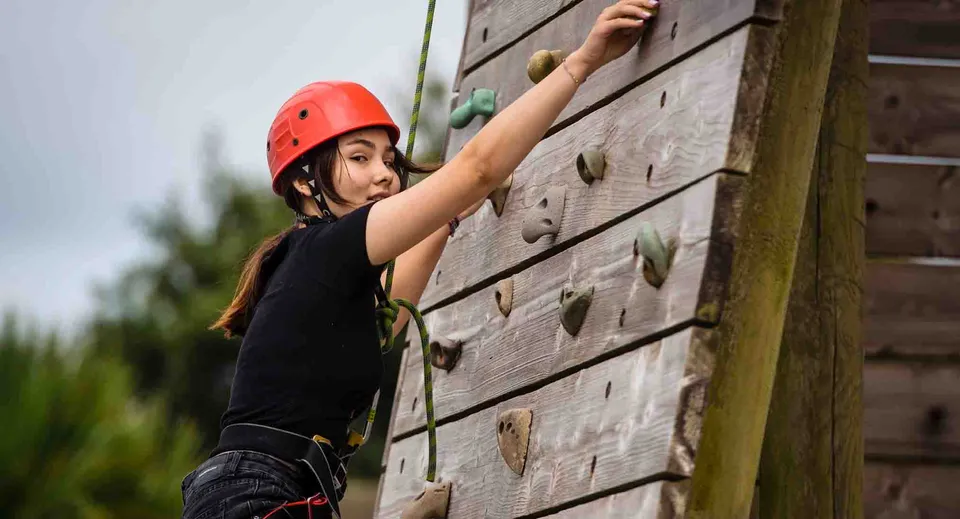 Una studentessa della Westbourne School si arrampica su una parete di legno all'aperto indossando un casco rosso, con uno sfondo verde.