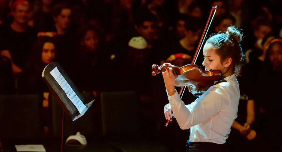 Una studentessa della King's School Rochester suona il violino sul palco davanti a un pubblico soffusamente illuminato.