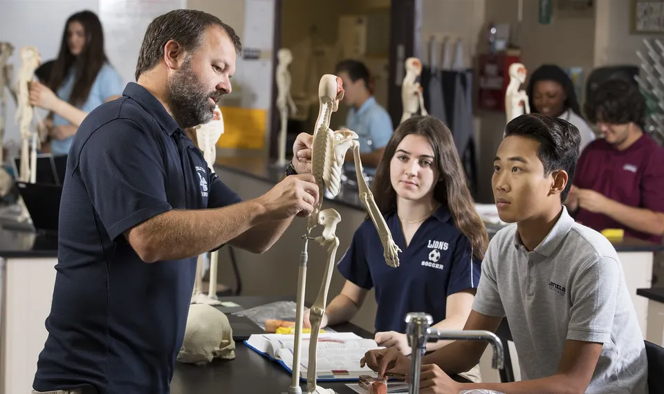 Un uomo sta davanti a un gruppo di studenti della Linfield Christian School e tiene un modello di scheletro durante la lezione di anatomia.