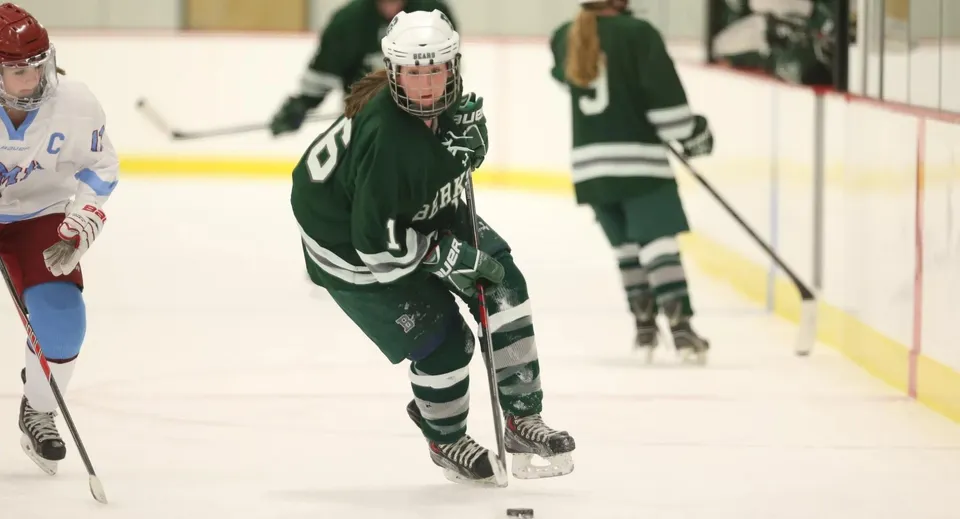 Due giocatori di hockey della Berkshire School in maglie verdi e bianche giocano sul ghiaccio di una pista.