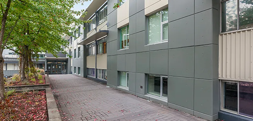 L'edificio a più piani della Windsor Secondary School con facciata grigia si trova lungo un viale pavimentato ed è circondato da alberi.