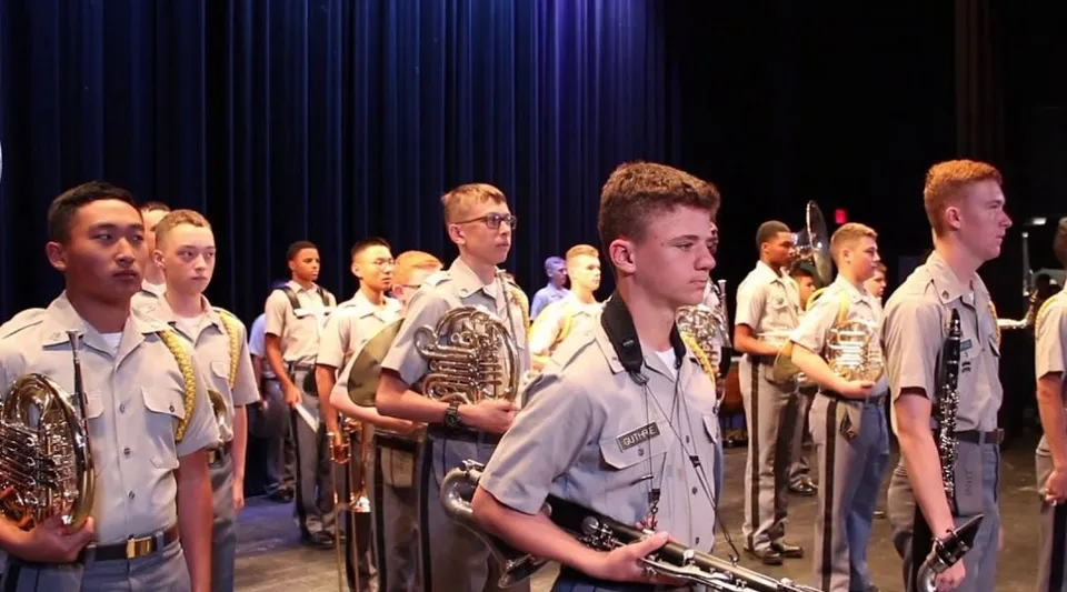 Studenti della Riverside Military Academy sono sul palco in uniforme davanti a un sipario scuro.