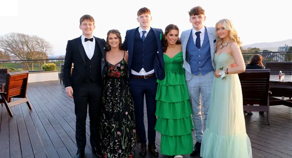 Un gruppo di persone in abito formale posa su una terrazza in legno con uno sfondo paesaggistico nel terreno della Sligo Grammar School.