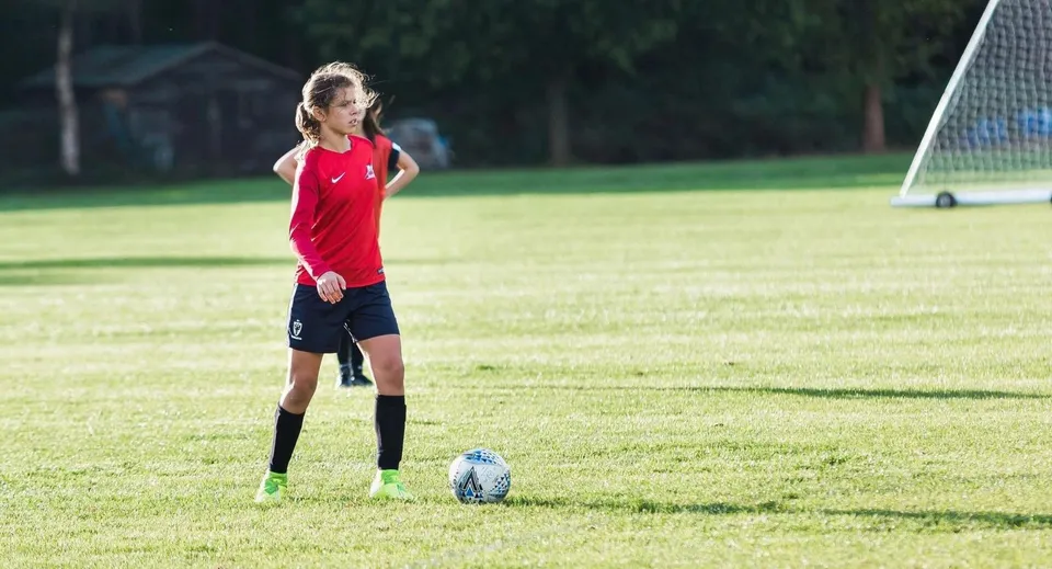Una giovane calciatrice della Marymount International School è sul campo da gioco con il pallone tra i piedi davanti a una porta.