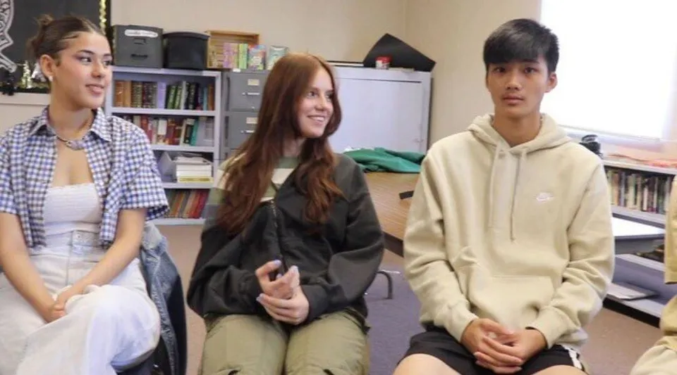 Tre studenti siedono nell'aula della Huntington High School circondati da scaffali con libri di testo.