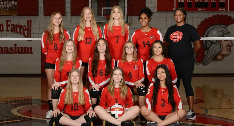 Un gruppo di giovani giocatrici di pallavolo in maglia rossa del Paradise Valley Unified School District posa in palestra.